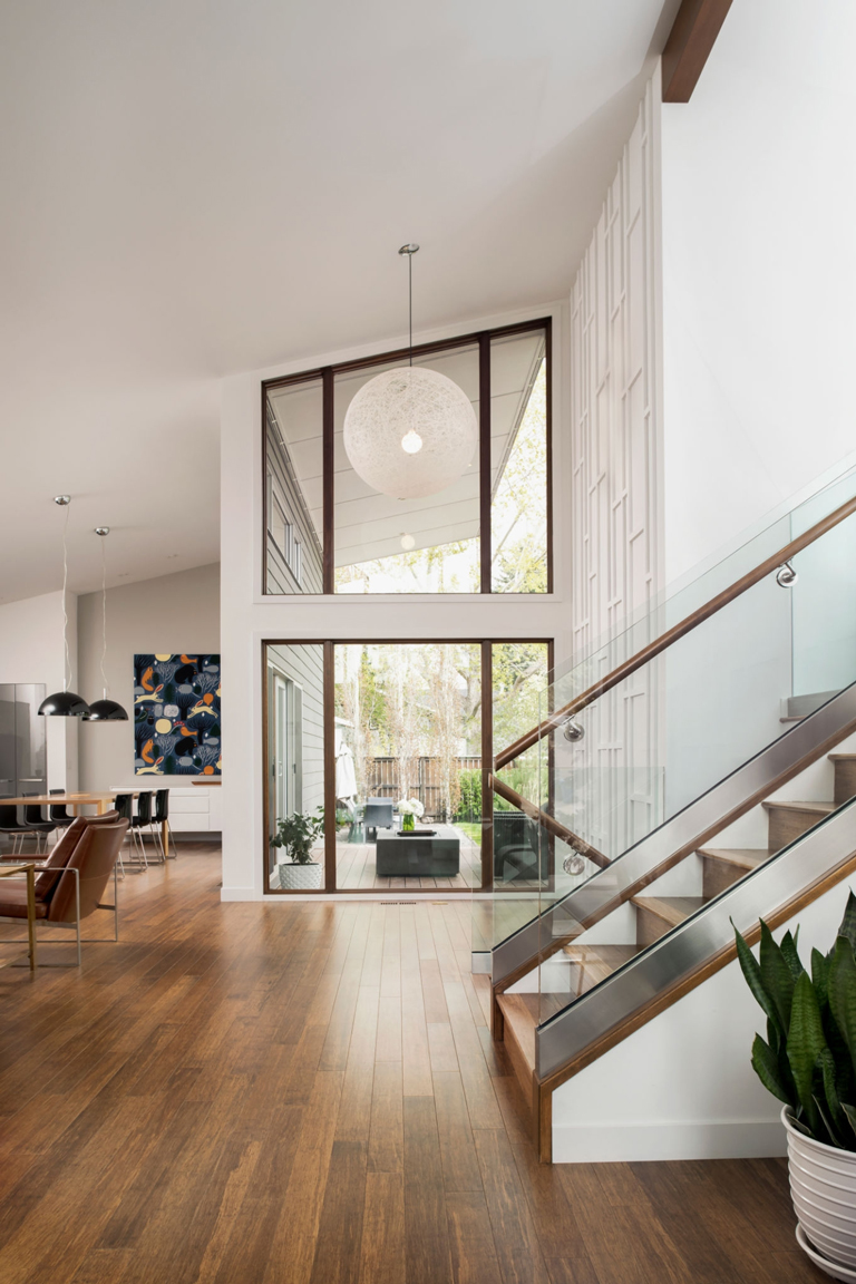 Escalera con baranda de vidrio, acceso principal con ventanales de doble altura y diseño interior moderno – FRANCO HomeServices