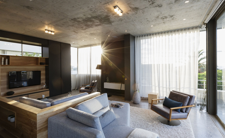 Sala de lujo con sofá modular, luz natural del atardecer, cortinas translúcidas y techo en concreto – FRANCO HomeServices